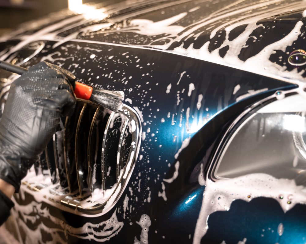 Detailed car wash. Detailing center worker cleans car's radiator grill with brush